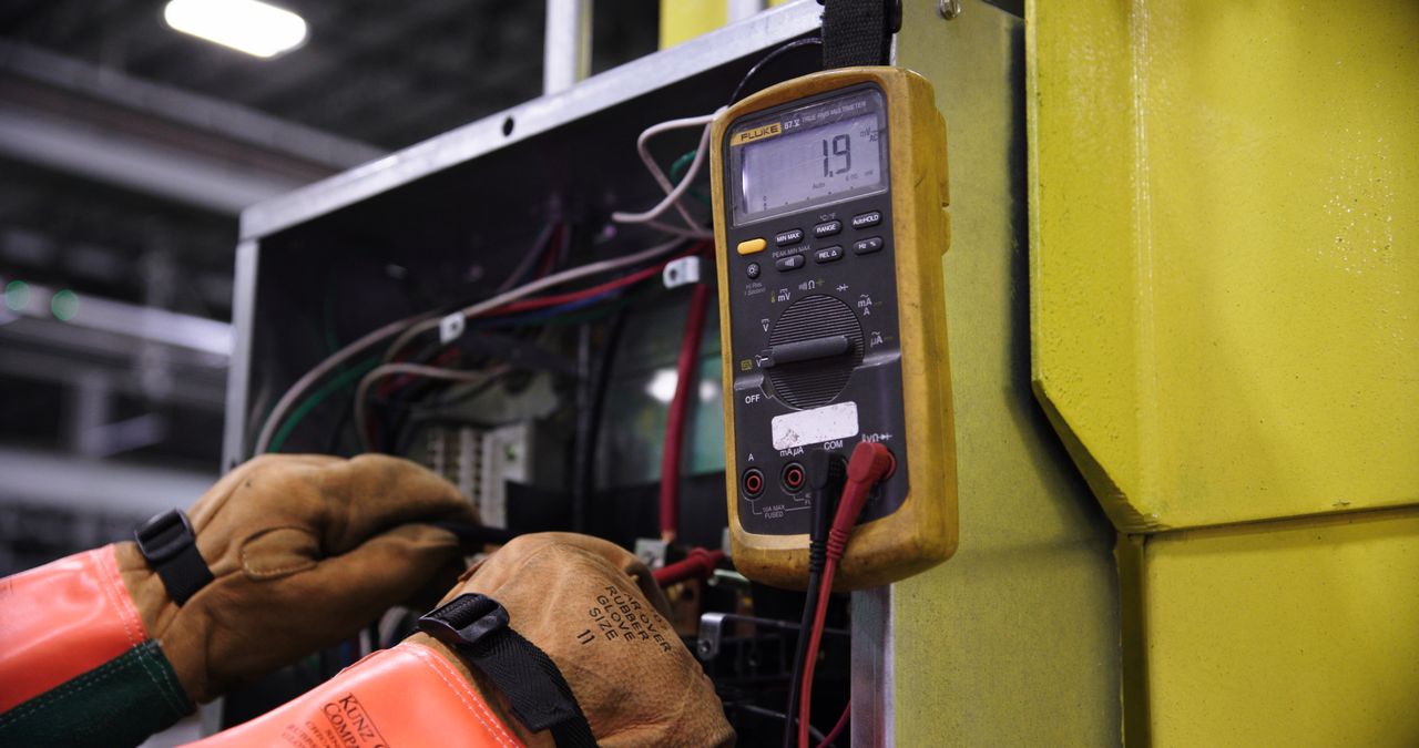 contact-img Electrician using a multimeter to fix industrial control panel wiring.