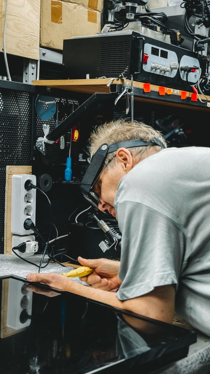 our-experience Professional technician working on electronic device repair in a cluttered workshop.