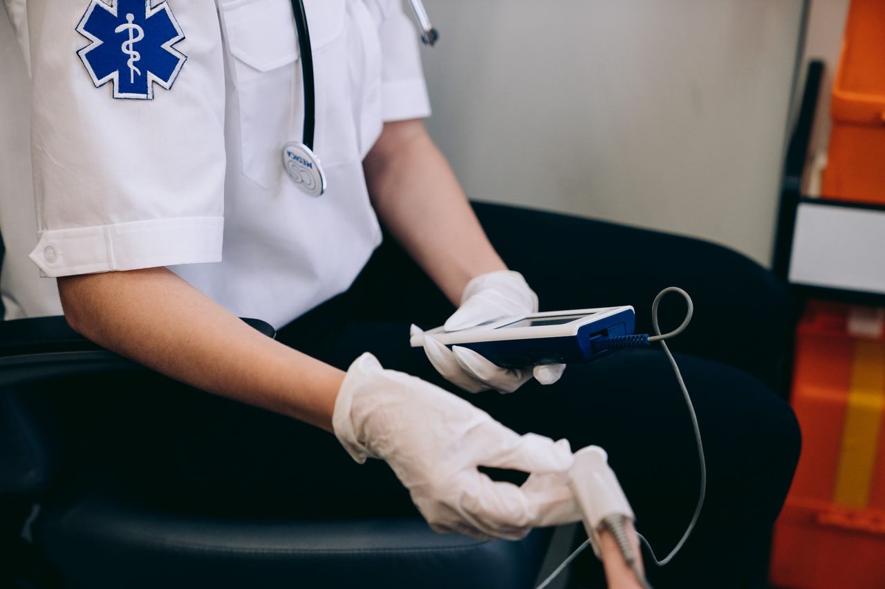 why-choose-us A paramedic monitors patient vitals using handheld medical equipment indoors.
